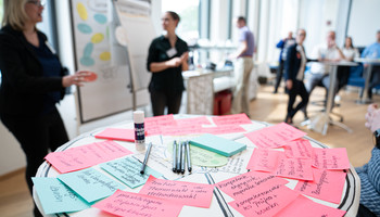 EduAction Expertenforum | © Freudenberg Gruppe Karten für die Pinnwand liegen auf einem Stehtisch im Hintergrund Menschen im Workshop | © Freudenberg Gruppe