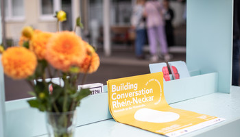 Der Matchbox-Infostand | © Arthur Bauer Blumen, Plakate und Flyer auf einem Infostand | © Arthur Bauer