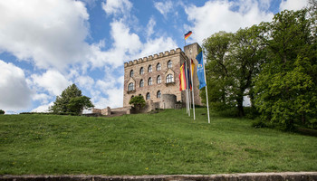 Das Hambacher Schloss | © Arthur Bauer Blick von unten auf das Hambacher Schloss, Flaggen wehen, schönes Wetter, grüne Wiese im Vordergrund | © Arthur Bauer