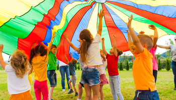 Kinder spielen | © Shutterstock Standard Lizenz Eine Gruppe Kinder spielt auf einer Wiese mit einer bunten Plane | © Shutterstock Standard Lizenz