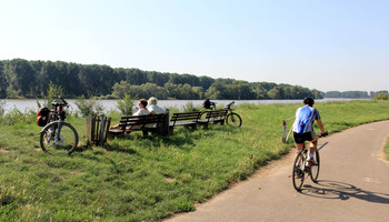 Regionalparkrouten | © VRRN \/ Pei Fahrradfahrer fährt am Rhein, daneben Sitzbänke mit Radfahrern die Pause machen | © VRRN \/ Pei
